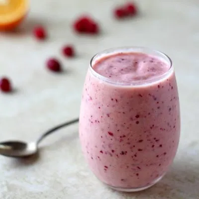 Cranberry and orange smoothie in a clear glass against a white background