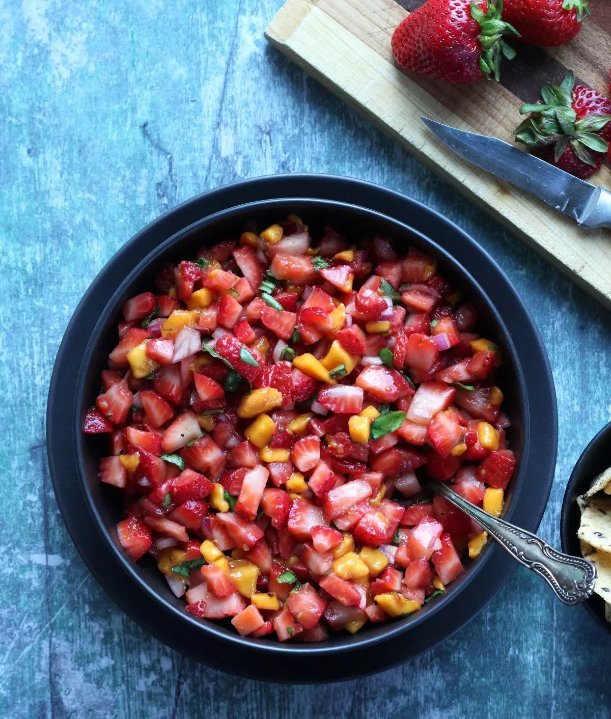 Diced strawberries as a salsa in a black bowl on a greenish background