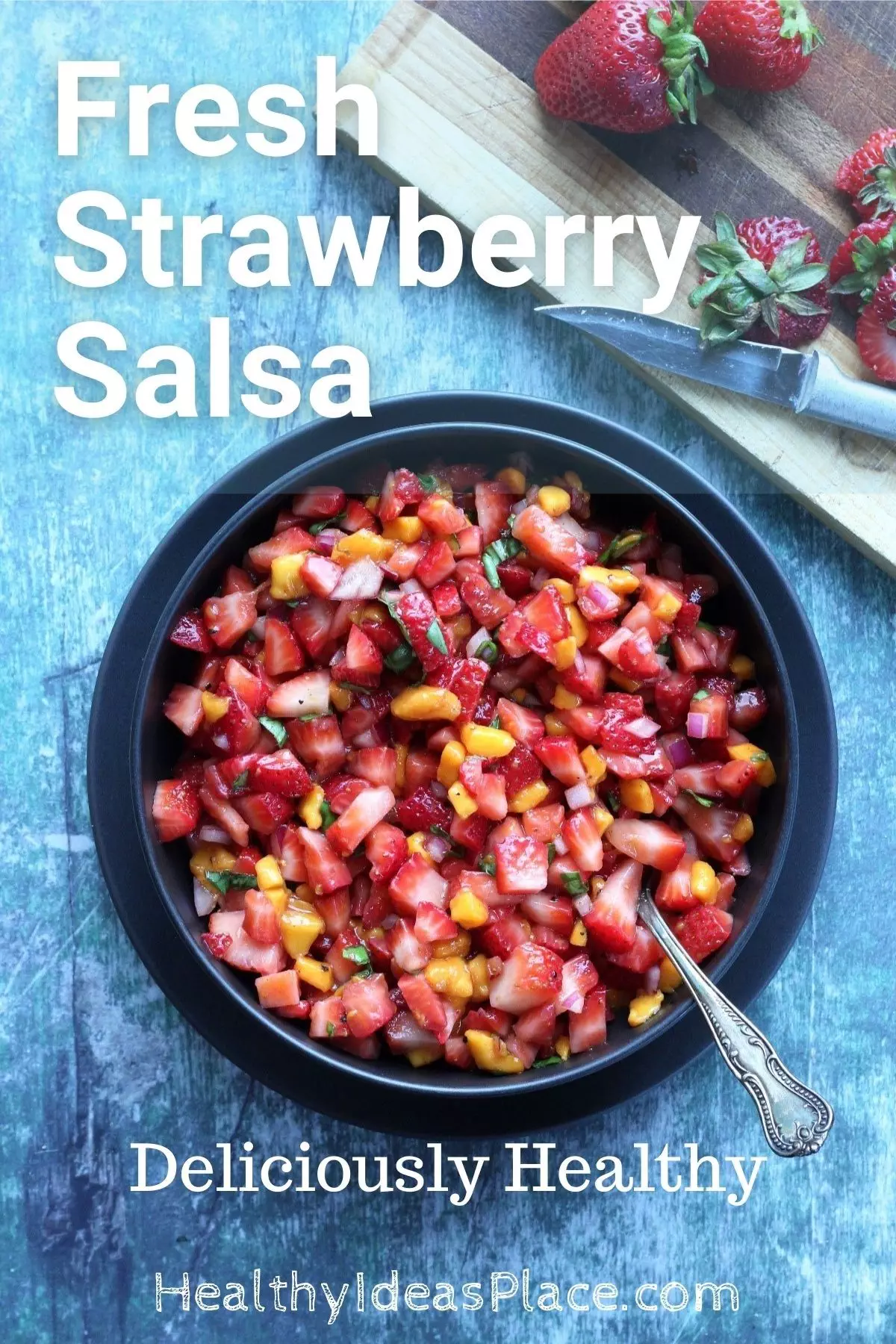 looking down on a black bowl of diced strawberries and mango on a greenish background