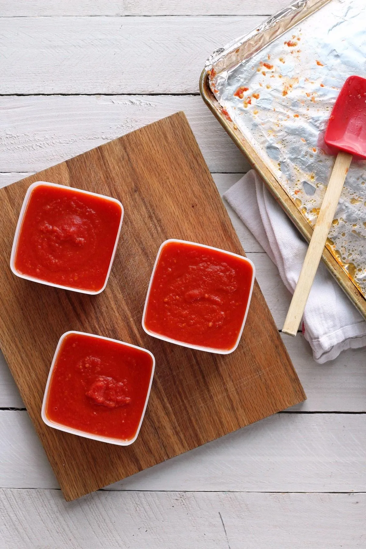 Homemade tomato sauce in plastic containers on wooden cutting board