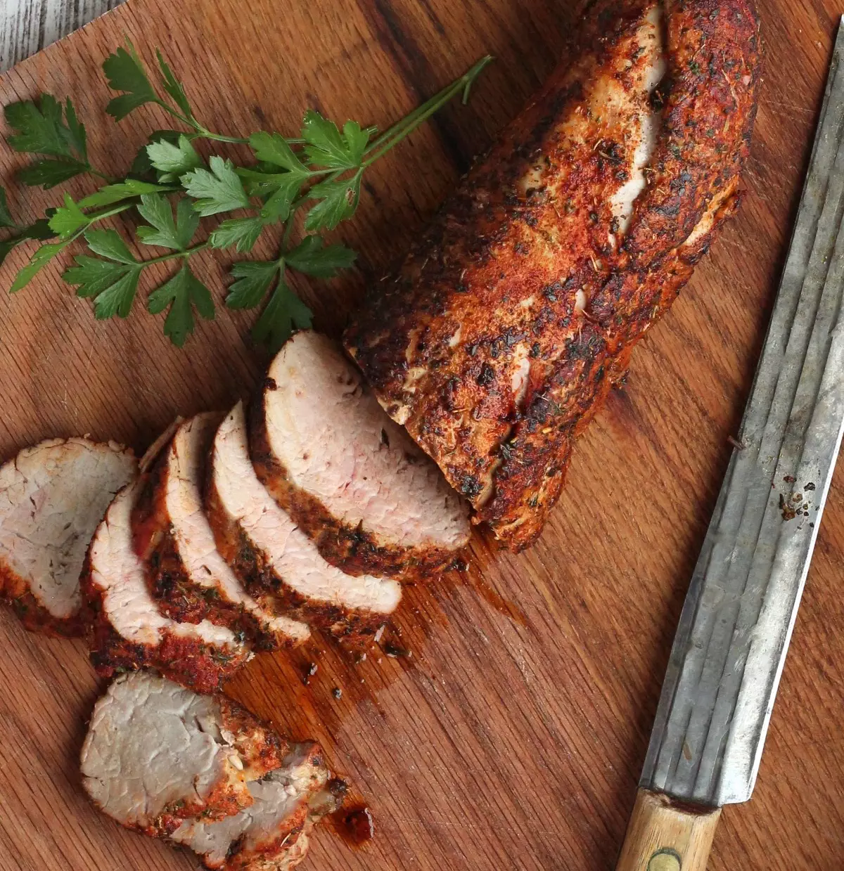 Sliced pork tenderloin and parsley on wood cutting board