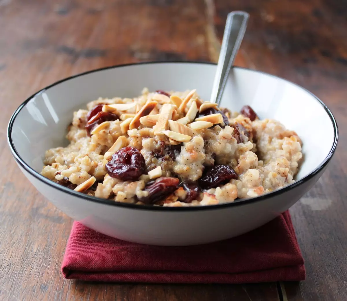 cooked oats with dried cherries and slivered almonds in white bowl against wood background