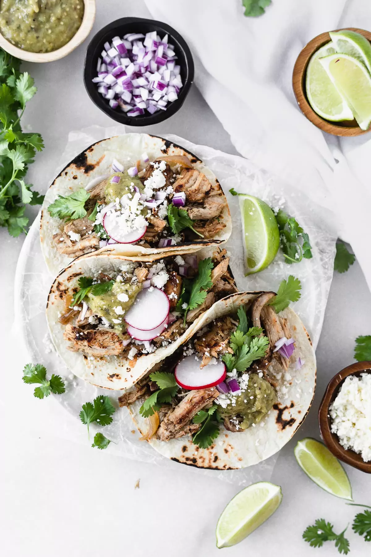 carnitas tacos on a white plate with toppings against a white background