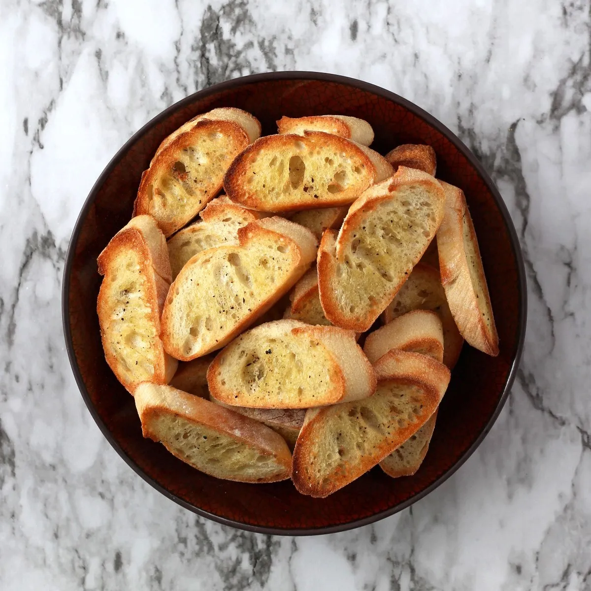 Crostini in brown bowl against white background