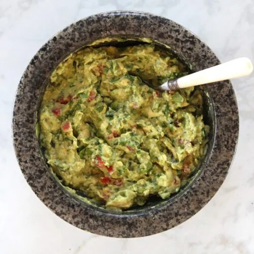 guacamole in stone bowl with white handled spoon