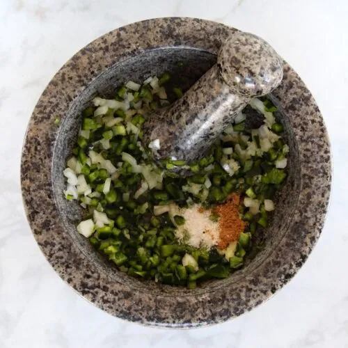 chopped onions and peppers with spices in a mortar and pestel
