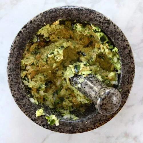 Mashed avocado with chopped peppers and onions in mortar and pestal